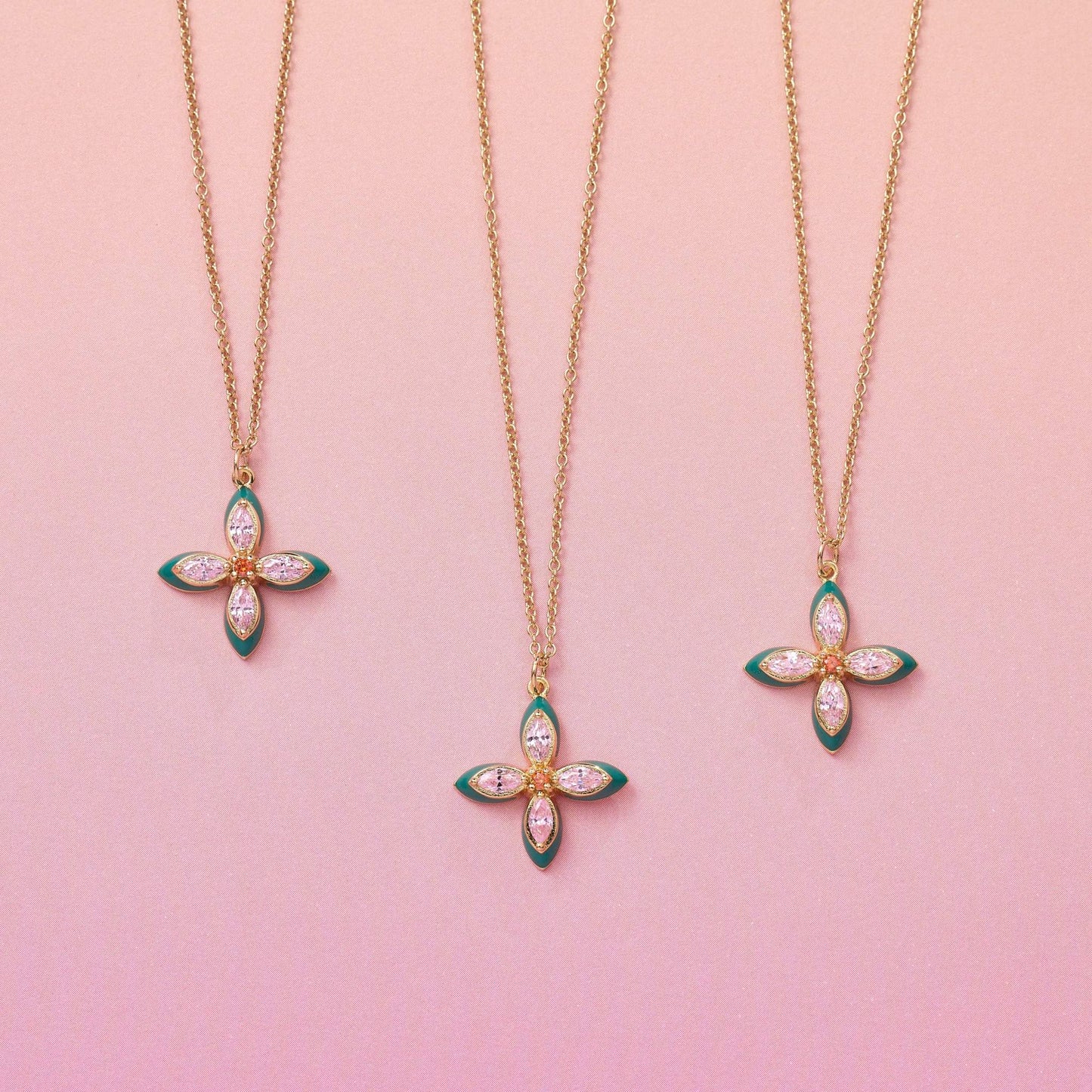 Three Lucky Clover Pendant Necklaces with emerald enamel and lab grown cubic zirconia on gold chains against pink background