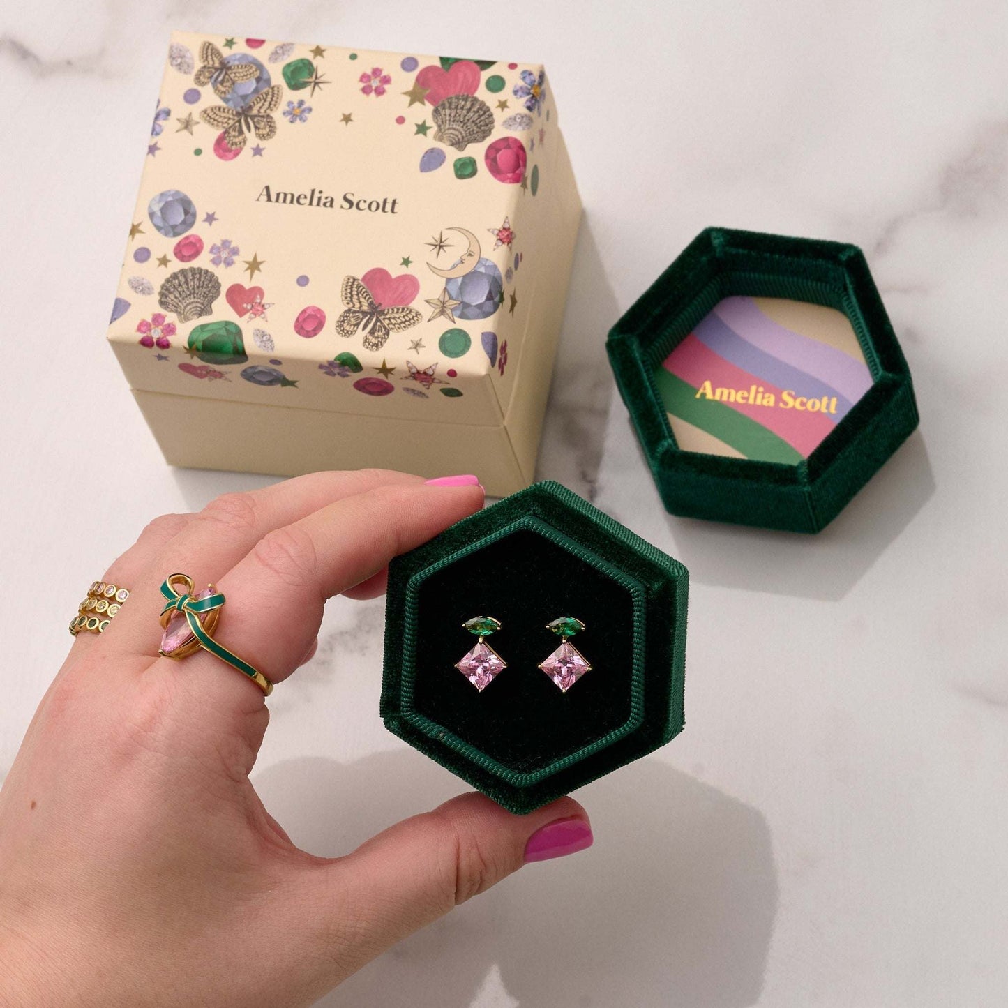Unusual gold earrings. Emerald green and pink cubic zirconia studs in green velvet box with floral gift packaging, hand holding box with matching ring