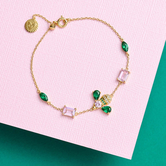 Beatrice Jewelled Bee Bracelet with emerald green, blush pink stones and gold-plated chain on pink and teal background