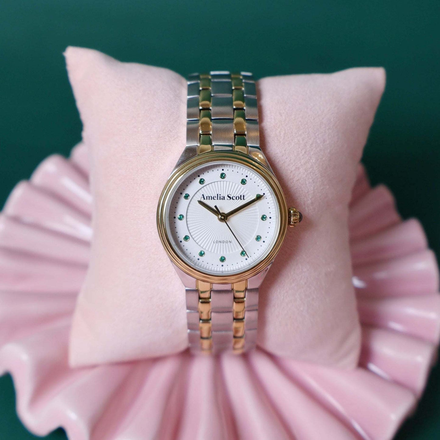 Silver and gold vintage style ladies watch on a pink cushion with a green background