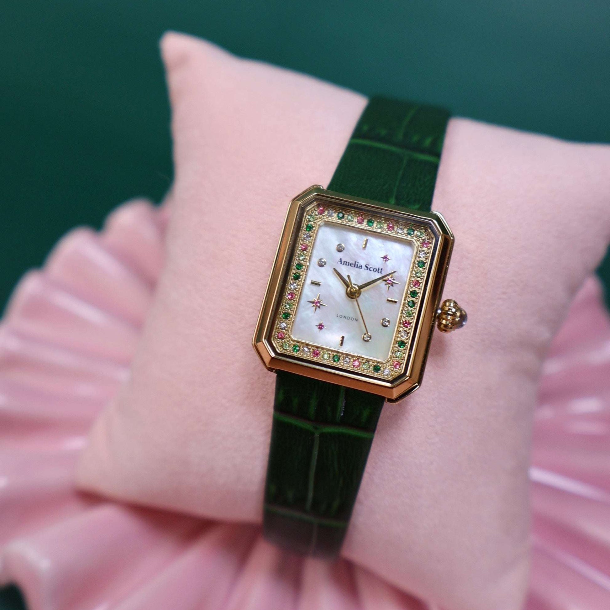 Luxury ladies watch with green croc vintage style leather strap on a pink cushion against a green background