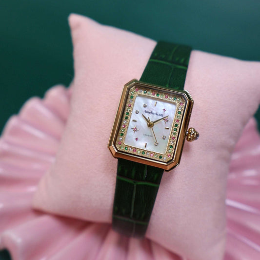 Luxury ladies watch with green croc vintage style leather strap on a pink cushion against a green background