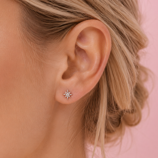 Close-up of an ear wearing a star-shaped earring against a pink background